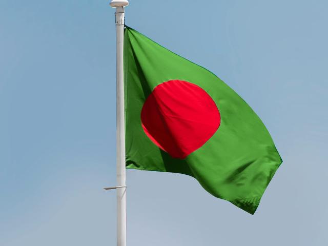 The flag of Bangladesh waving outside over a blue sky